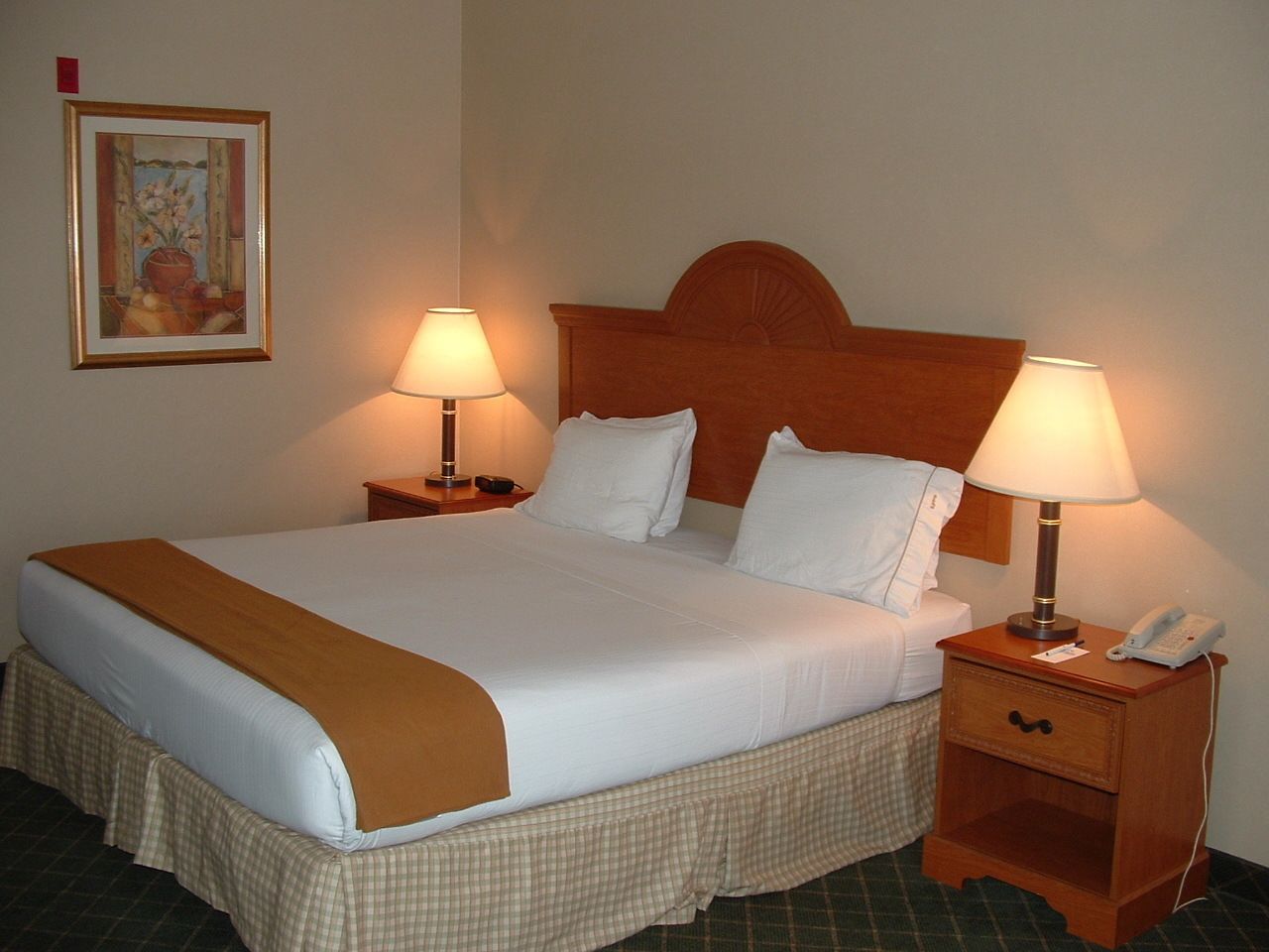 A neatly made bed with a brown throw blanket, two bedside lamps, a bedside phone, and a small wooden nightstand.