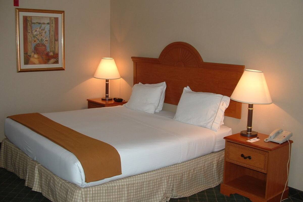 A neatly made bed with a brown throw blanket, two bedside lamps, a bedside phone, and a small wooden nightstand.