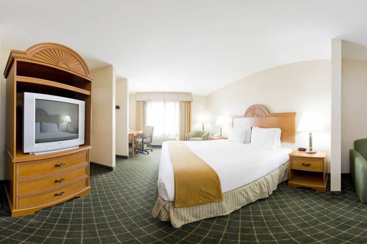 A hotel room with a bed, a television, a desk, a chair, and a sofa.