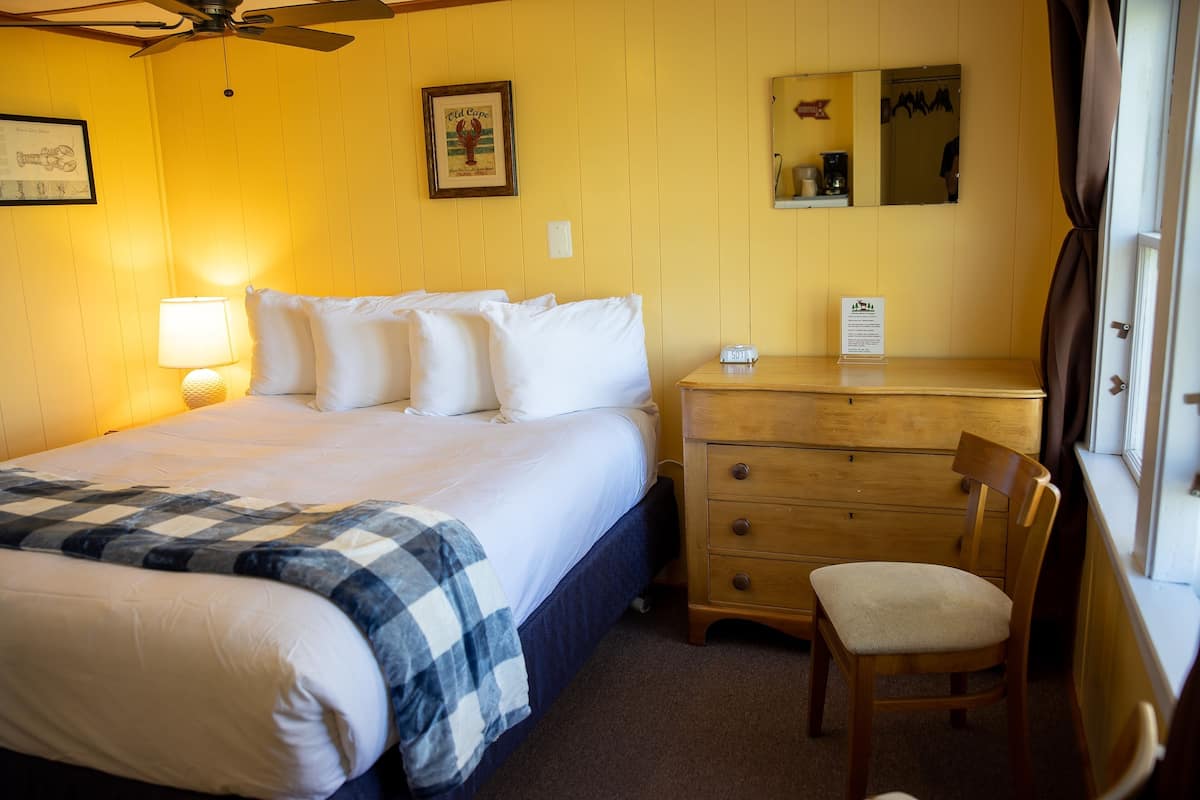 A hotel room with a bed, a wooden dresser, a chair, a lamp, and a mirror.