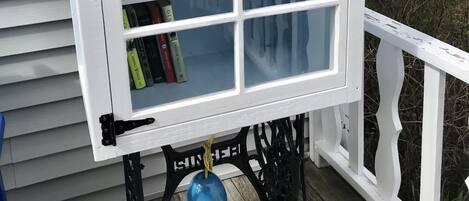 A small, white bookcase with a sign that reads "Little Library: Take a book, leave a book." It is mounted on a black metal stand with a rope tied around it.