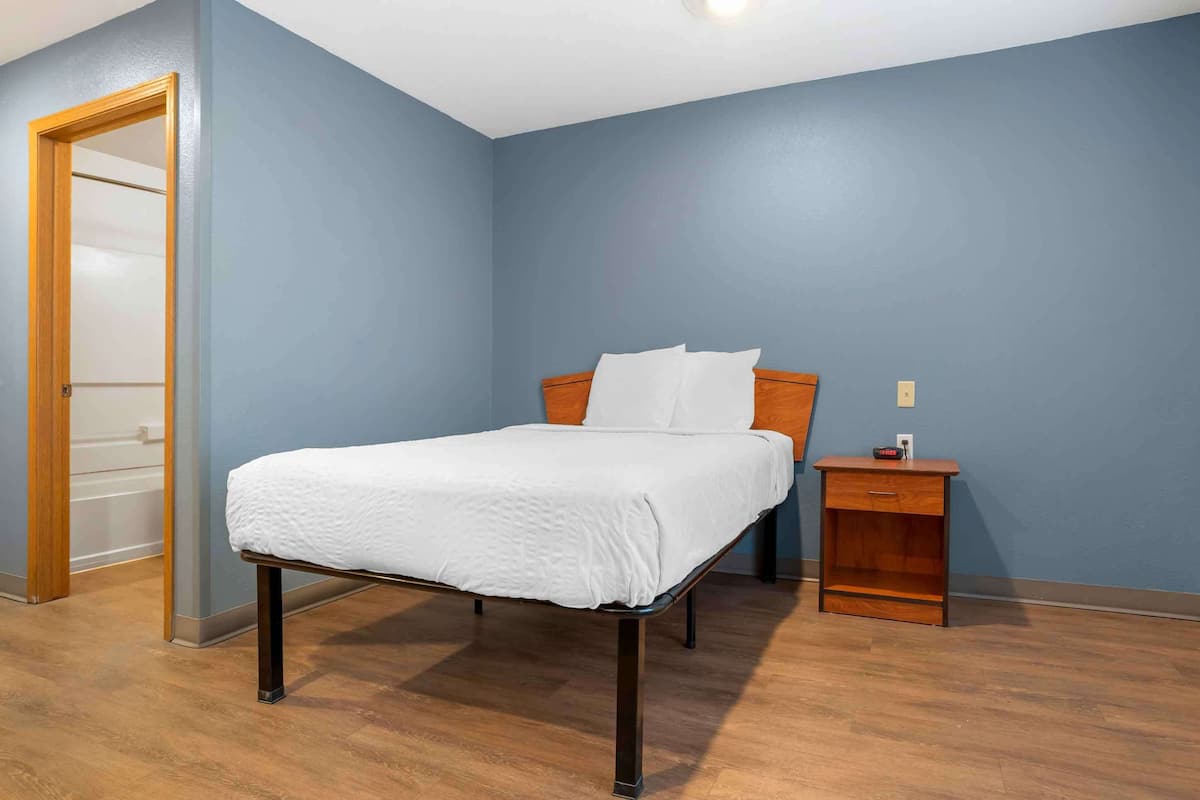 A bedroom with a bed, wooden nightstand, and a door.