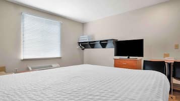 Ein Hotelzimmer mit einem großen Bett, einem Flachbildfernseher, einem Schreibtisch mit Stuhl und einem Fenster mit Jalousien.