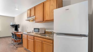 A compact kitchen with wooden cabinets, a microwave, a sink, and a white Whirlpool refrigerator.