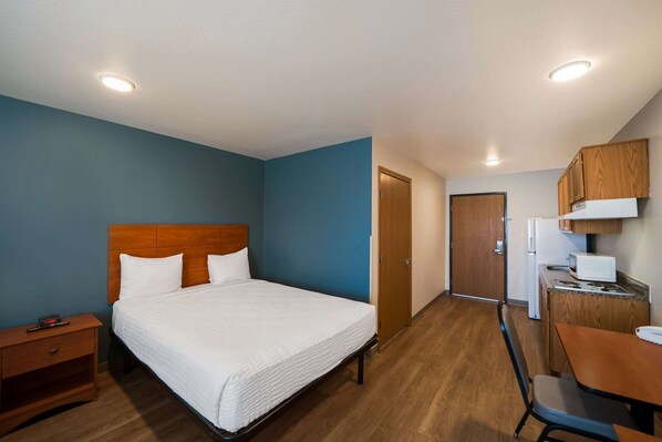 A hotel room with a bed, a desk, a microwave, and a refrigerator.