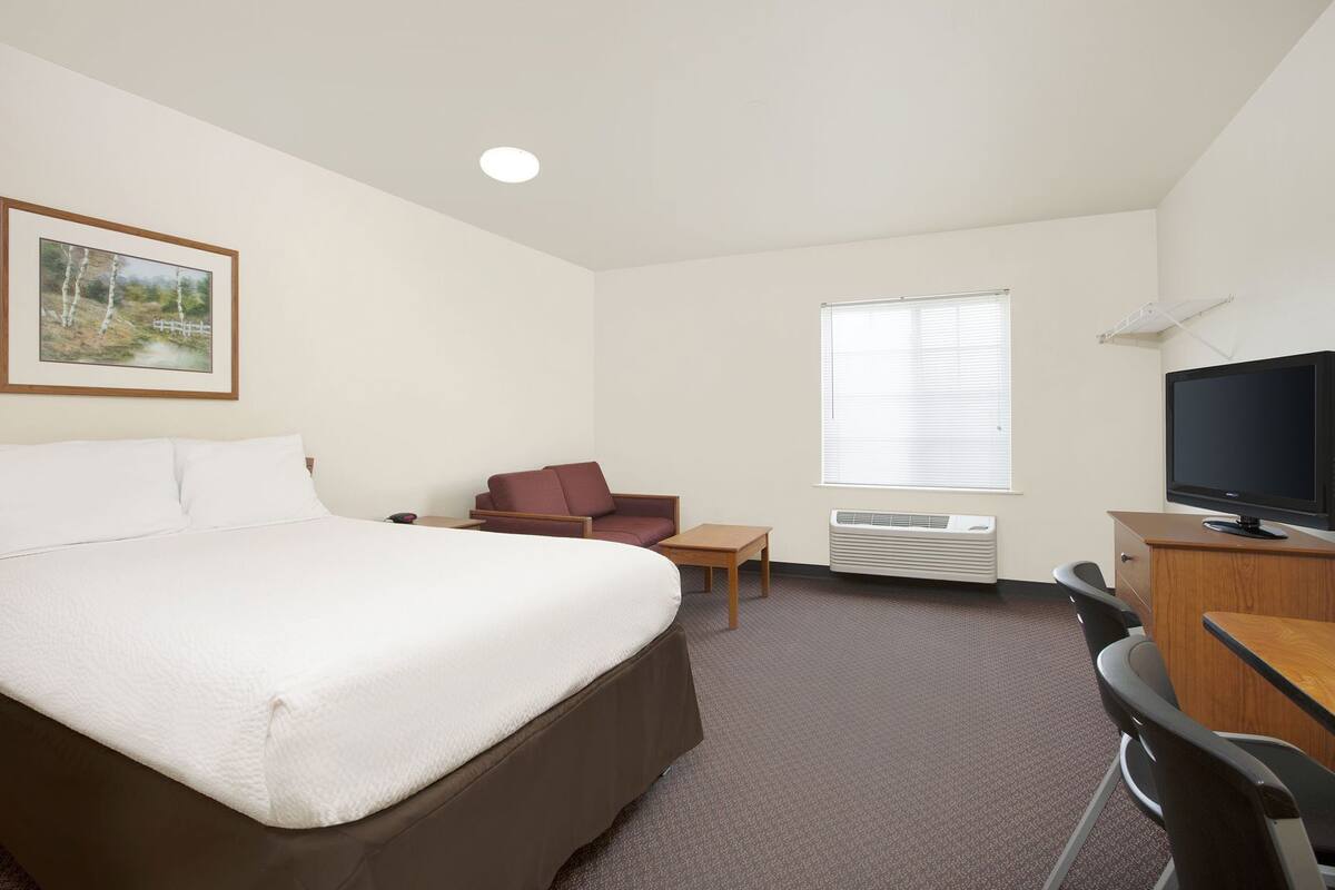 A hotel room with a bed, a desk, a chair, a television, and an air conditioning unit.