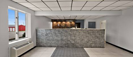 A reception area with a marble counter, a patterned rug, and a view of a red building outside.