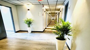 A long, narrow hallway with a wooden floor, potted plants, and an exit sign on the ceiling. - Quality Inn & Suites Caribou (Caribou)
