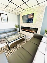 Una sala de estar moderna con pared de piedra, televisor de pantalla plana, chimenea y zona de estar con una mesa de centro de vidrio.