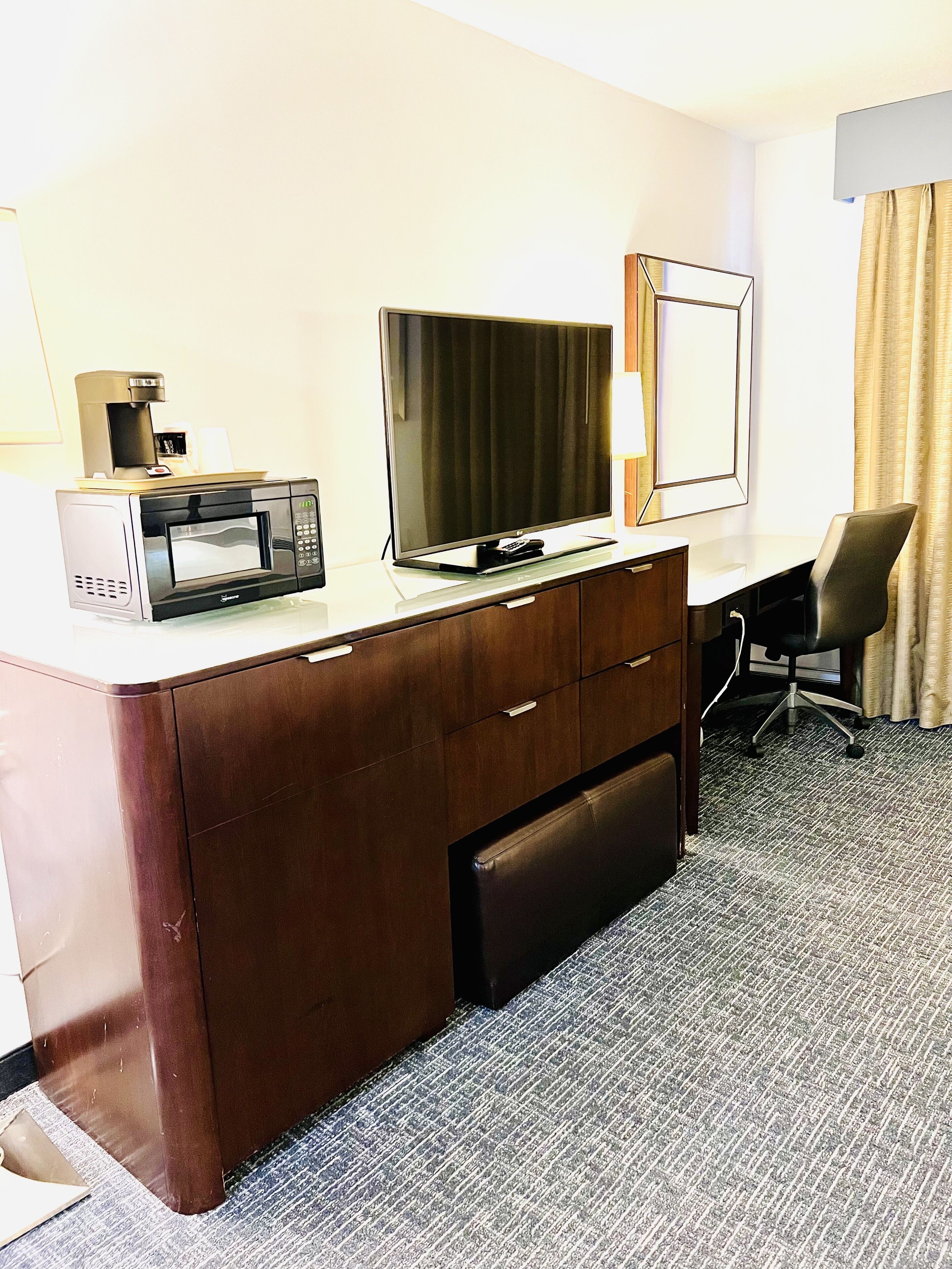 Una habitación de hotel con un escritorio de madera, un televisor de pantalla plana, una cafetera y una silla.