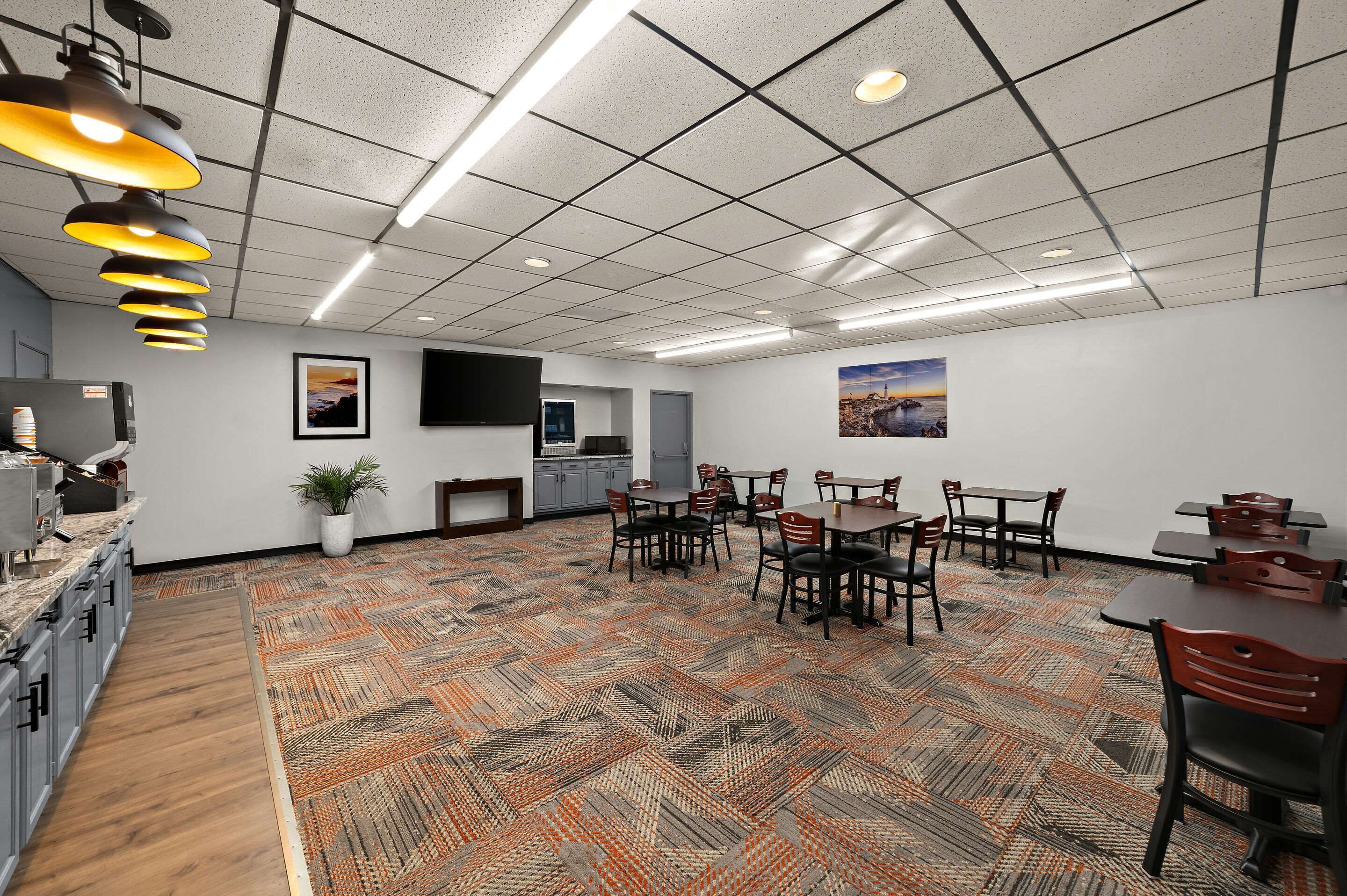 Une salle de conférence dotée d’un tapis à motifs, de plusieurs tables et chaises, d’un téléviseur à écran plat et d’une plante en pot.