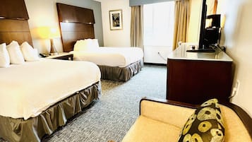 Habitación de hotel con dos camas, un escritorio, una silla y un ventanal con cortinas.