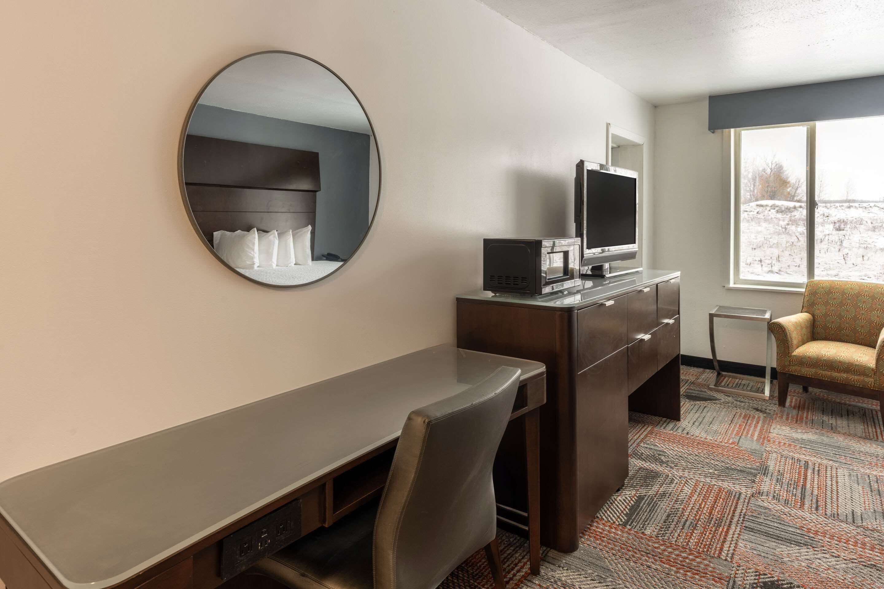 Ein Hotelzimmer mit Schreibtisch, Stuhl, Fernseher und einem großen Fenster.