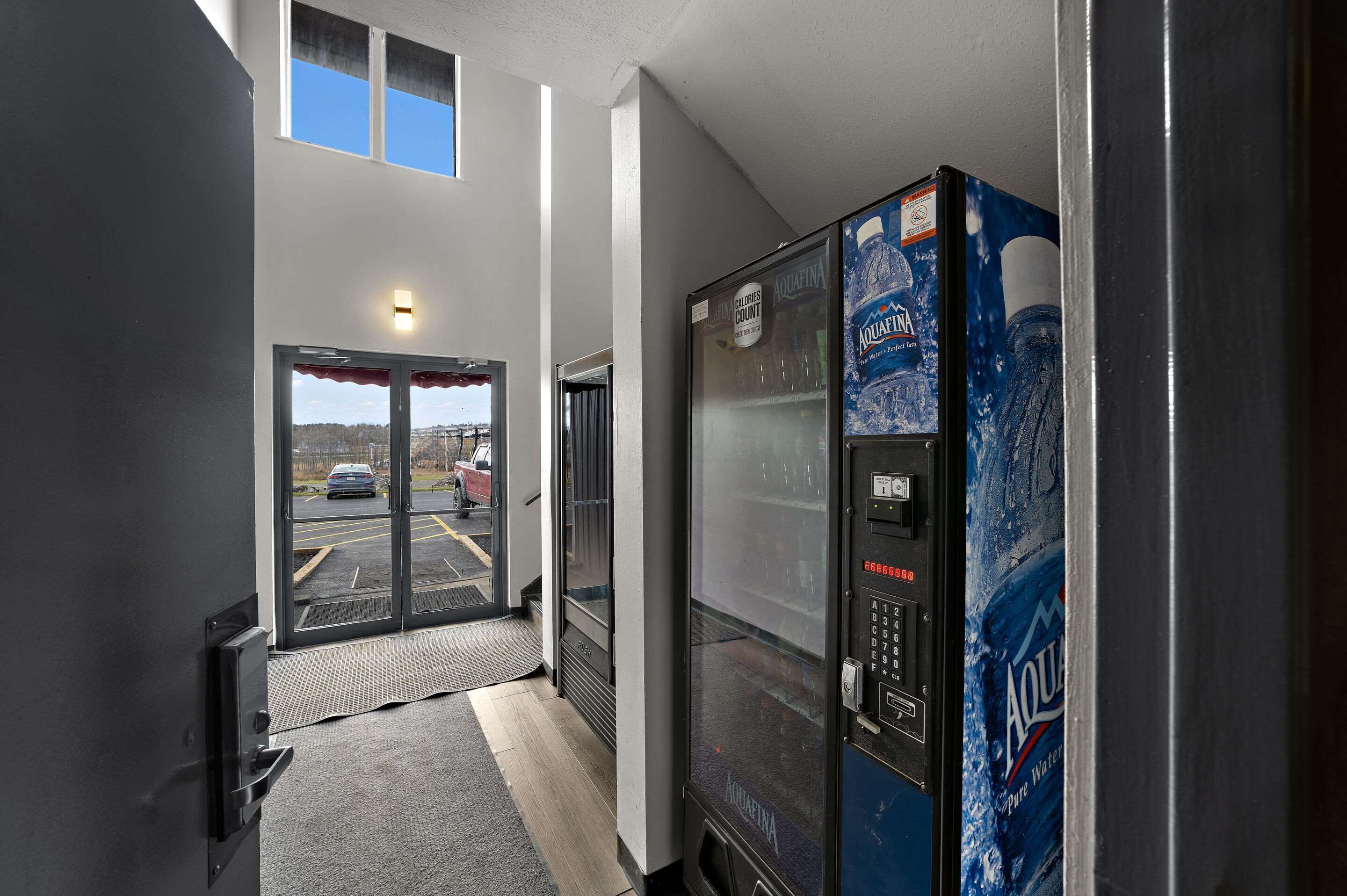 A hallway with a vending machine, a door leading to a parking lot, and a view of the outside.