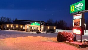 A hotel with a green sign, a parking lot, and a snow-covered ground.