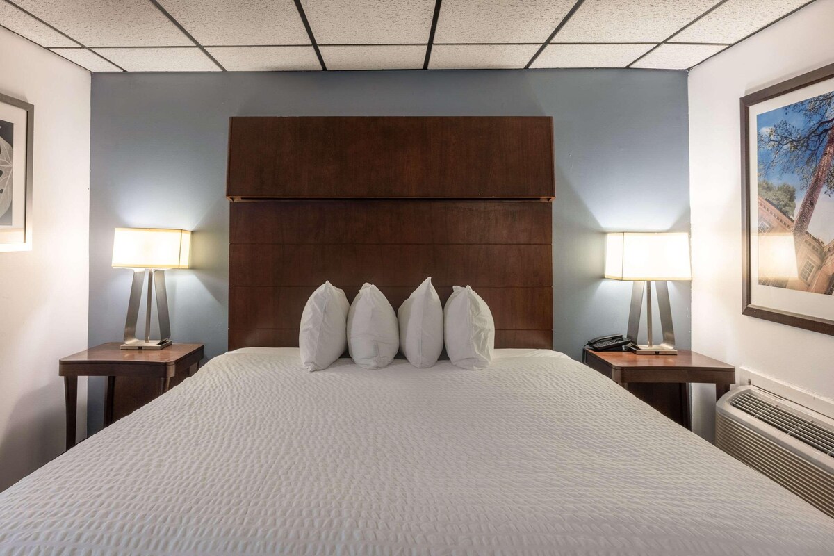 A hotel room with a large bed, a wooden headboard, two bedside tables with lamps, and a framed picture on the wall.