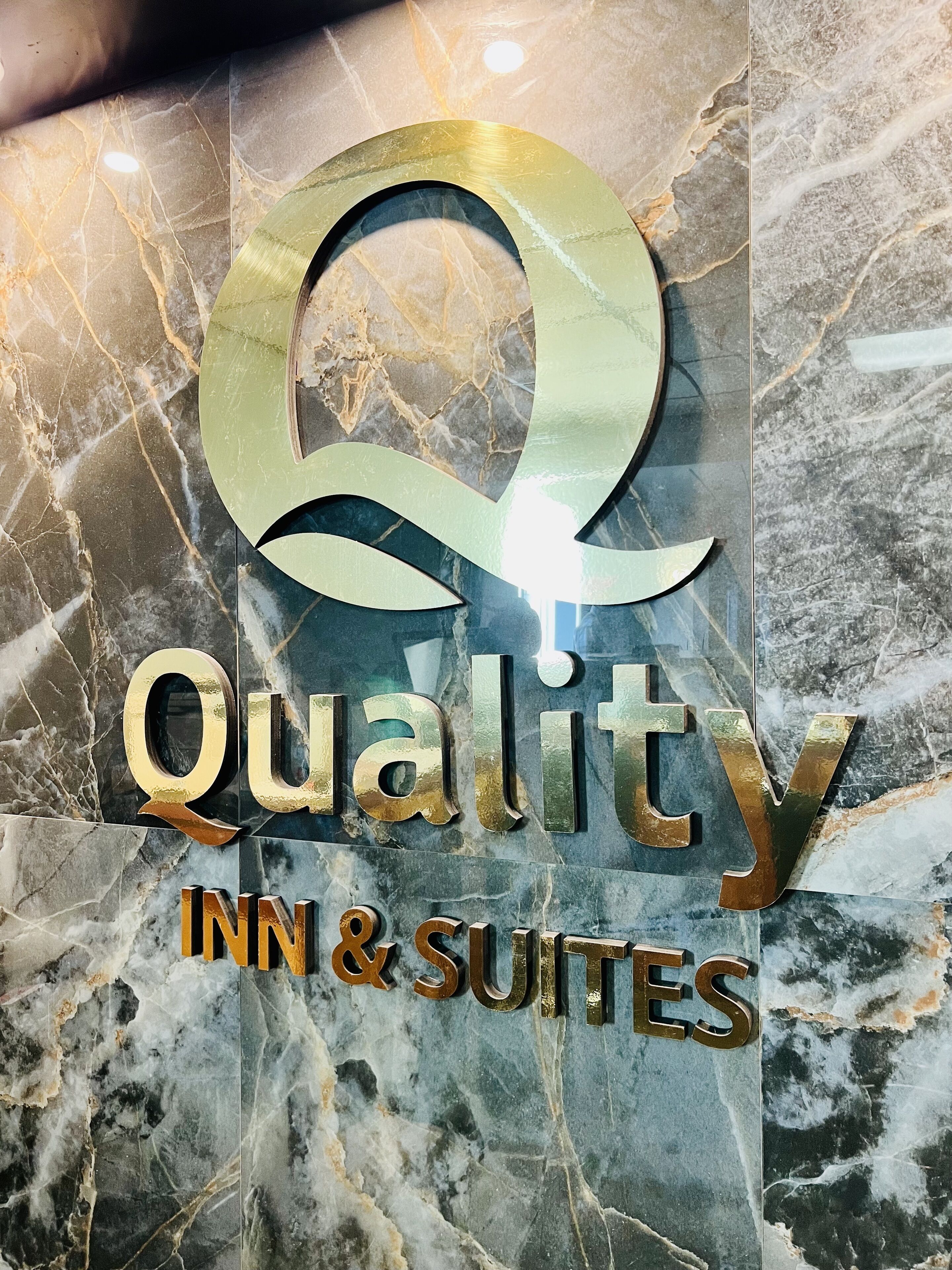 Une enseigne avec le logo et le nom « Quality Inn & Suites » sur un fond en marbre.