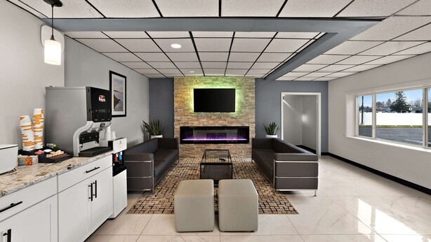 A modern living room with a fireplace, seating area, and kitchen counter with coffee machines. - Quality Inn & Suites Caribou (Caribou)