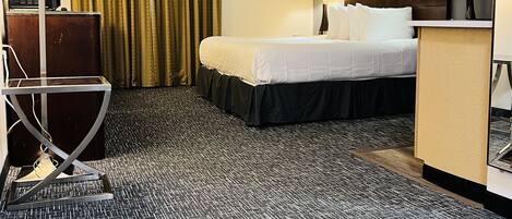 Une chambre d’hôtel avec un lit, un bureau, une chaise, une lampe, un tableau au mur et un luminaire au plafond.