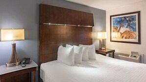 A hotel room with a large bed, two bedside tables with lamps, a telephone, a framed picture on the wall, and a built-in heater.