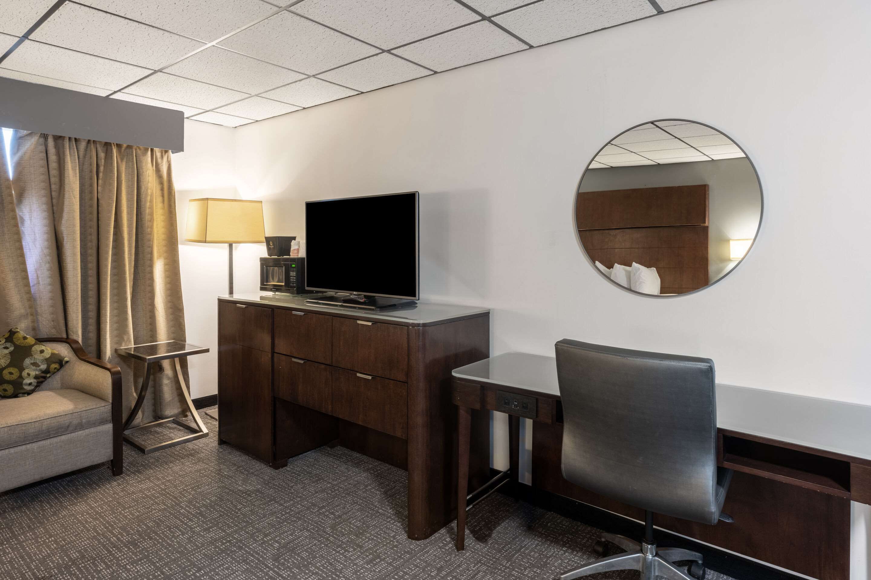 Habitación de hotel con sofá, escritorio, televisión, lámpara y espejo.