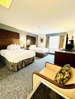 Habitación de hotel con dos camas, un escritorio, una silla y un televisor.