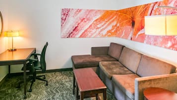 A room with a desk, chair, sofa, and a lamp.