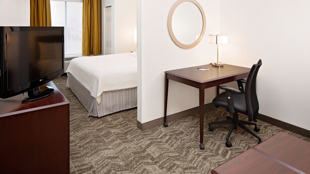 A hotel room with a bed, a desk with a chair, a television, and a round mirror on the wall.