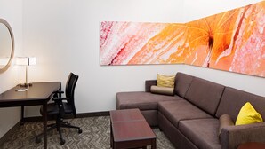 A modern hotel room with a desk, office chair, sofa, and a small wooden table.