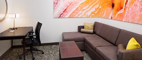 A modern hotel room with a desk, office chair, sofa, and a small wooden table.