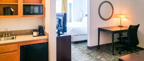 A hotel room with a kitchenette, a bed, a desk, and a lamp.