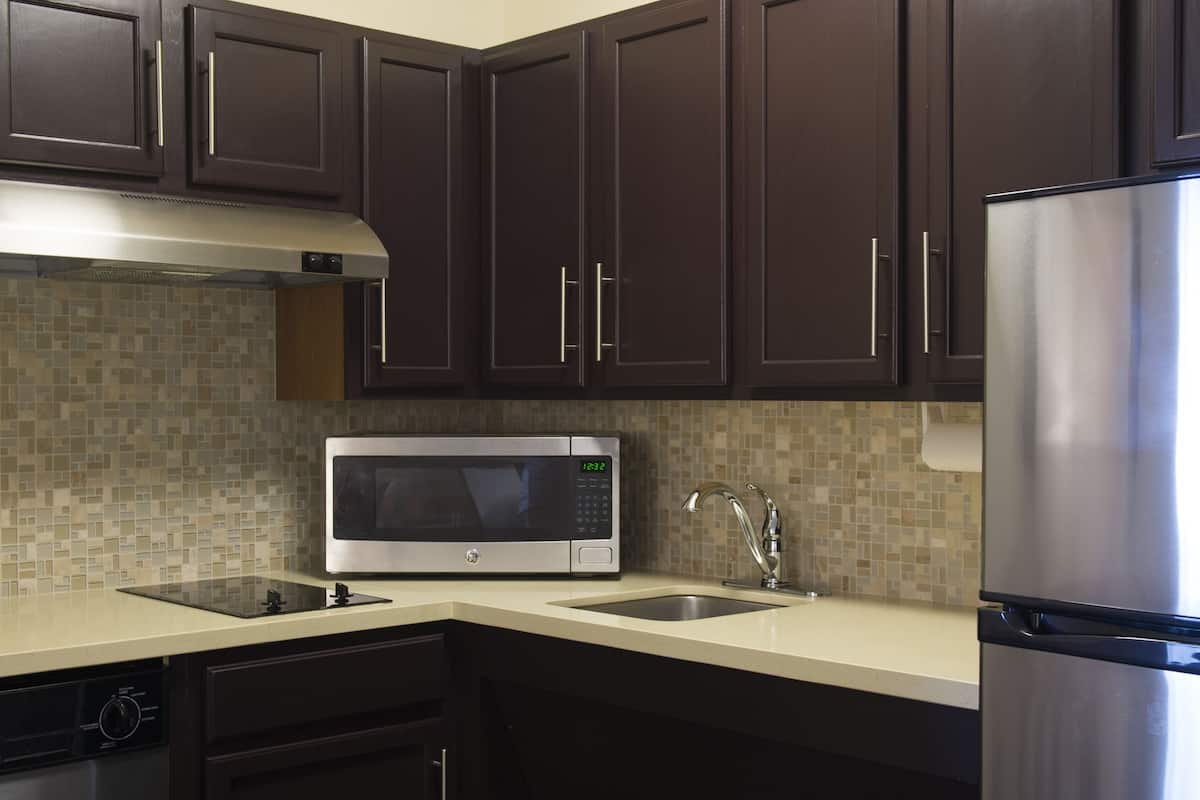 A modern kitchen with dark brown cabinets, a stainless steel refrigerator, a microwave, and a sink.