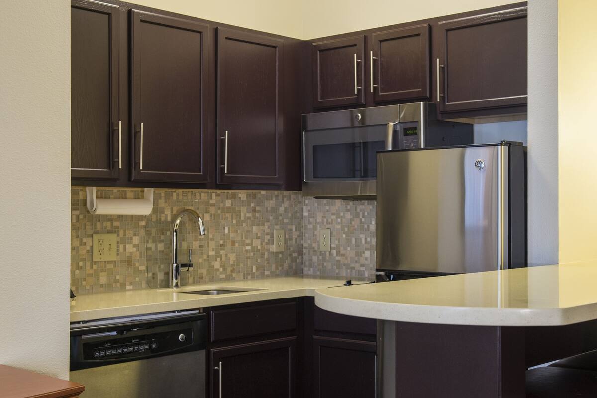 A modern kitchen with dark brown cabinets, stainless steel appliances, a tiled backsplash, and a built-in dishwasher.