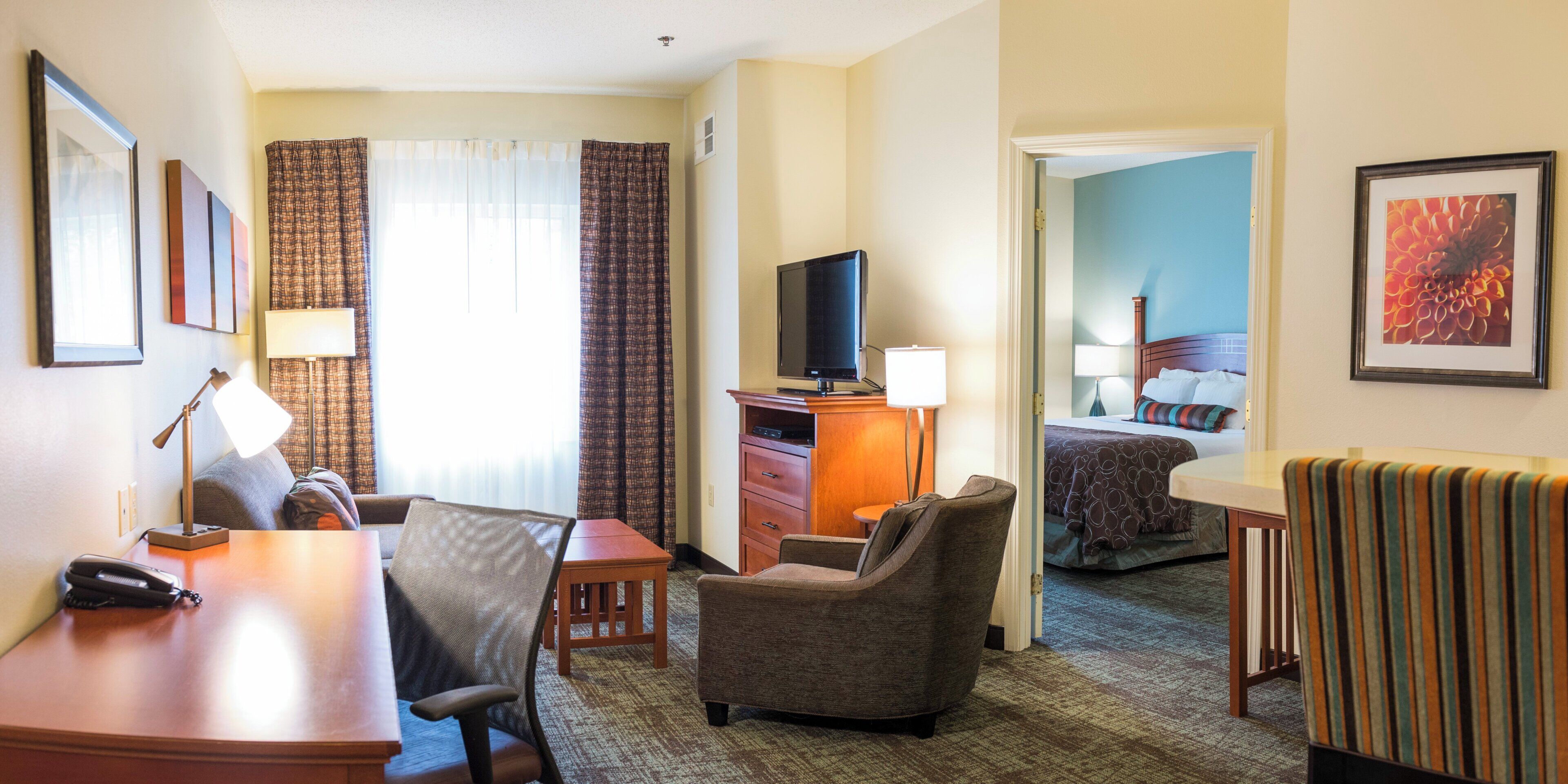 Una habitación de hotel con escritorio, silla, televisor y una cama con cabecera.