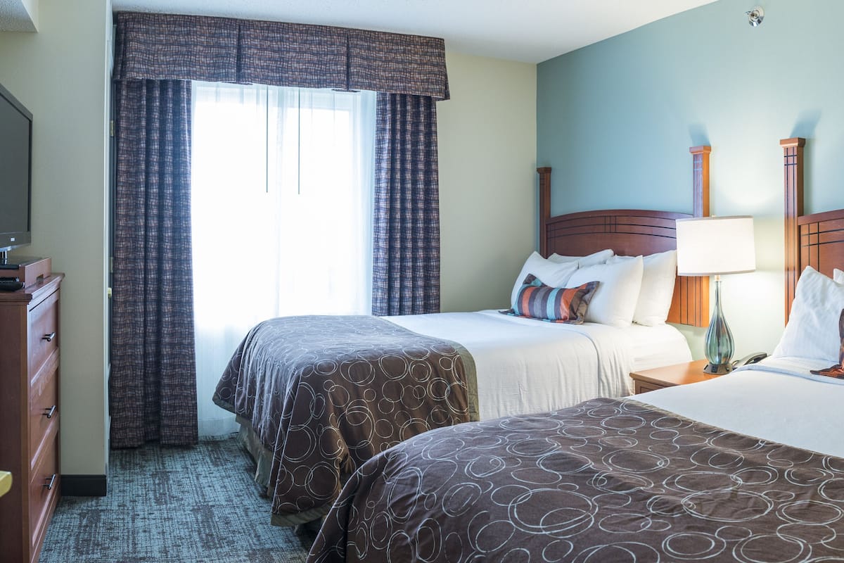 A hotel room with two beds, a television, a dresser, and a window with curtains.