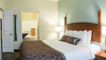 A hotel room with a bed, a nightstand, a lamp, and a door leading to a bathroom.