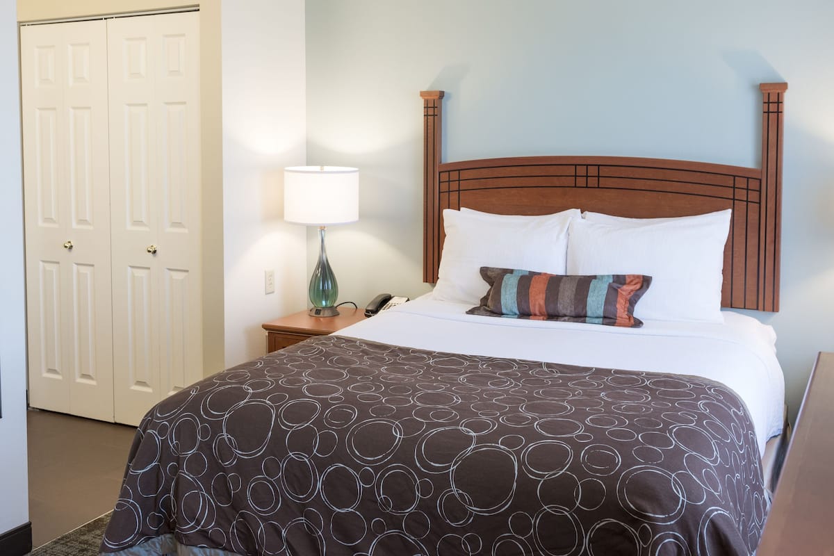 A hotel room with a large bed, a wooden headboard, two bedside lamps, a nightstand, and a mirror.