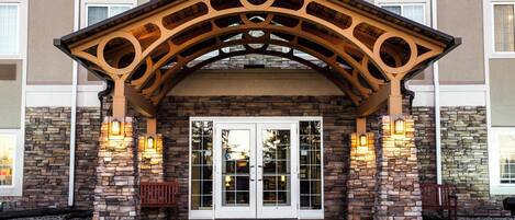 A hotel entrance with a stone facade, a wooden archway, and two illuminated wall sconces.