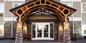 A hotel entrance with a stone facade, a wooden archway, and two illuminated wall sconces. - Staybridge Suites Fargo by IHG (Fargo)