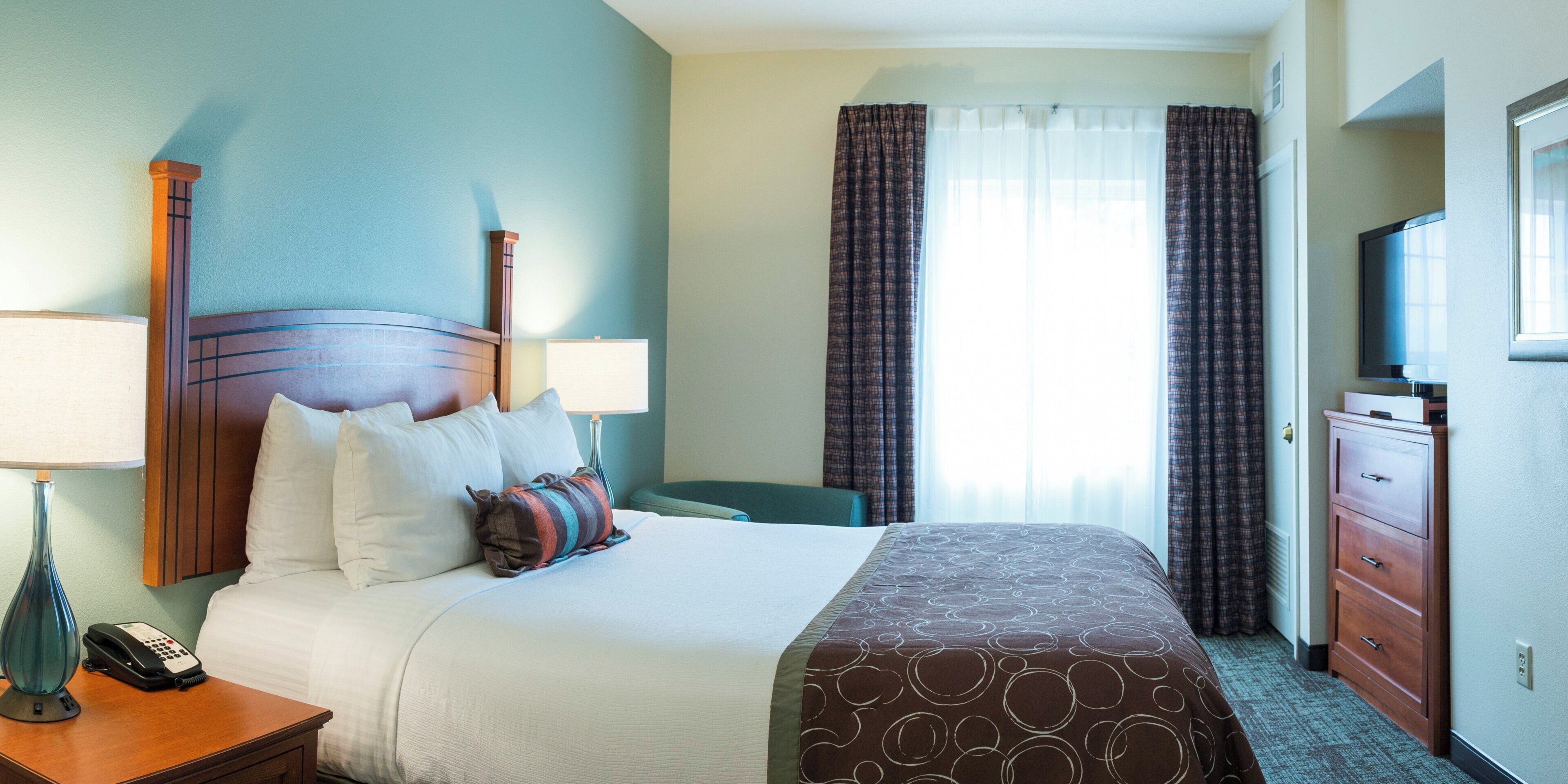 A hotel room with a bed, bedside lamps, a telephone, a television, and a window with curtains.