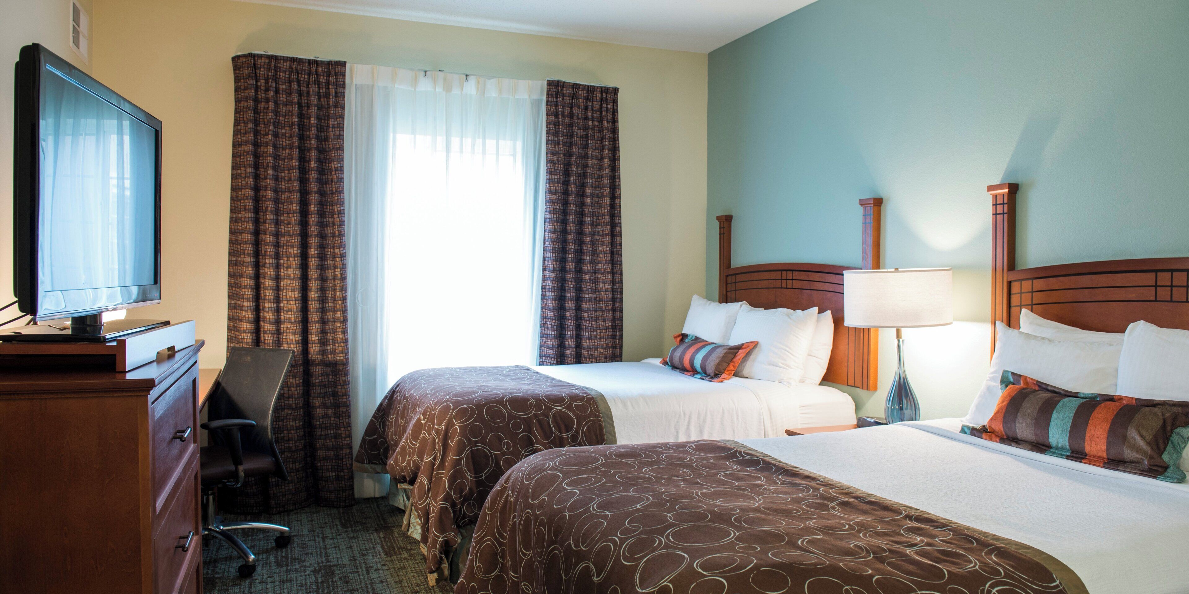 A hotel room with two beds, a desk with a television, and a chair.