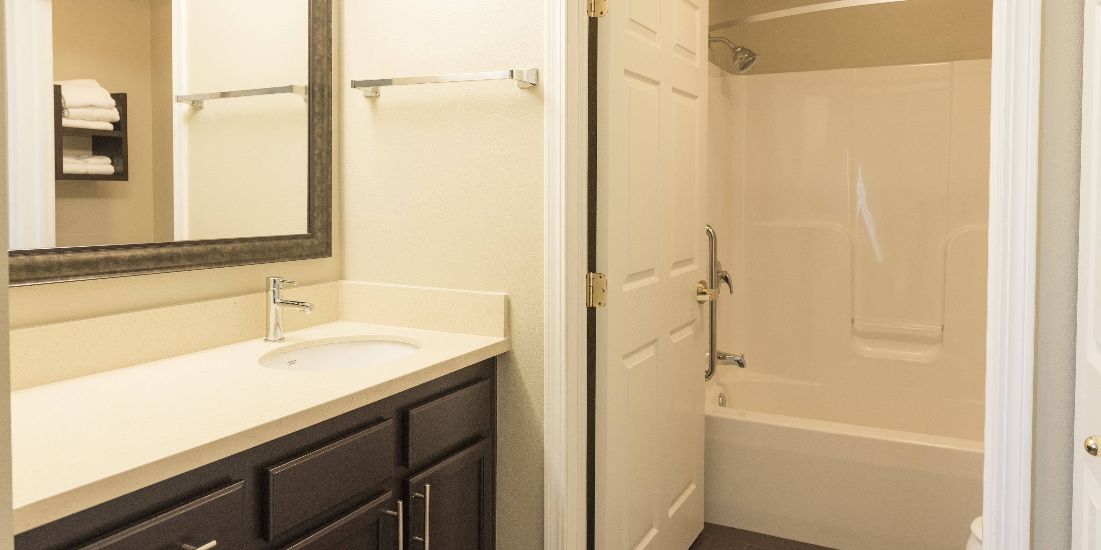 A bathroom with a sink, mirror, dark cabinets, and a shower area.