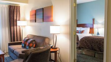 A hotel room with a sofa, a small table, a lamp, and a bed with a headboard.