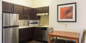A compact kitchen with dark cabinets, a stainless steel refrigerator, a microwave, and a dishwasher. There's a small dining table with a chair. - Staybridge Suites Fargo by IHG (Fargo)