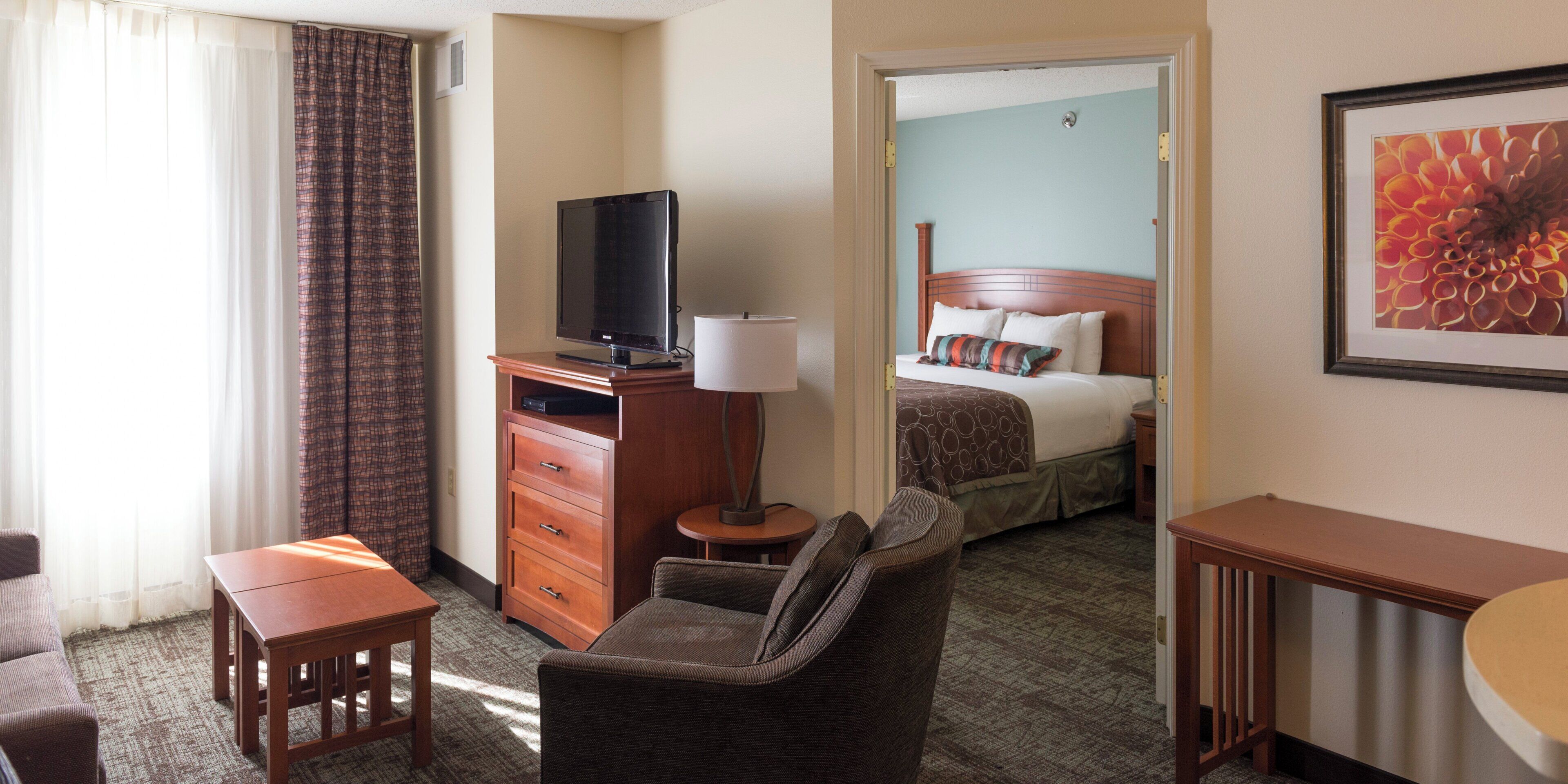 A hotel room with a television, a desk, a chair, a bed with pillows, and a framed picture on the wall.
