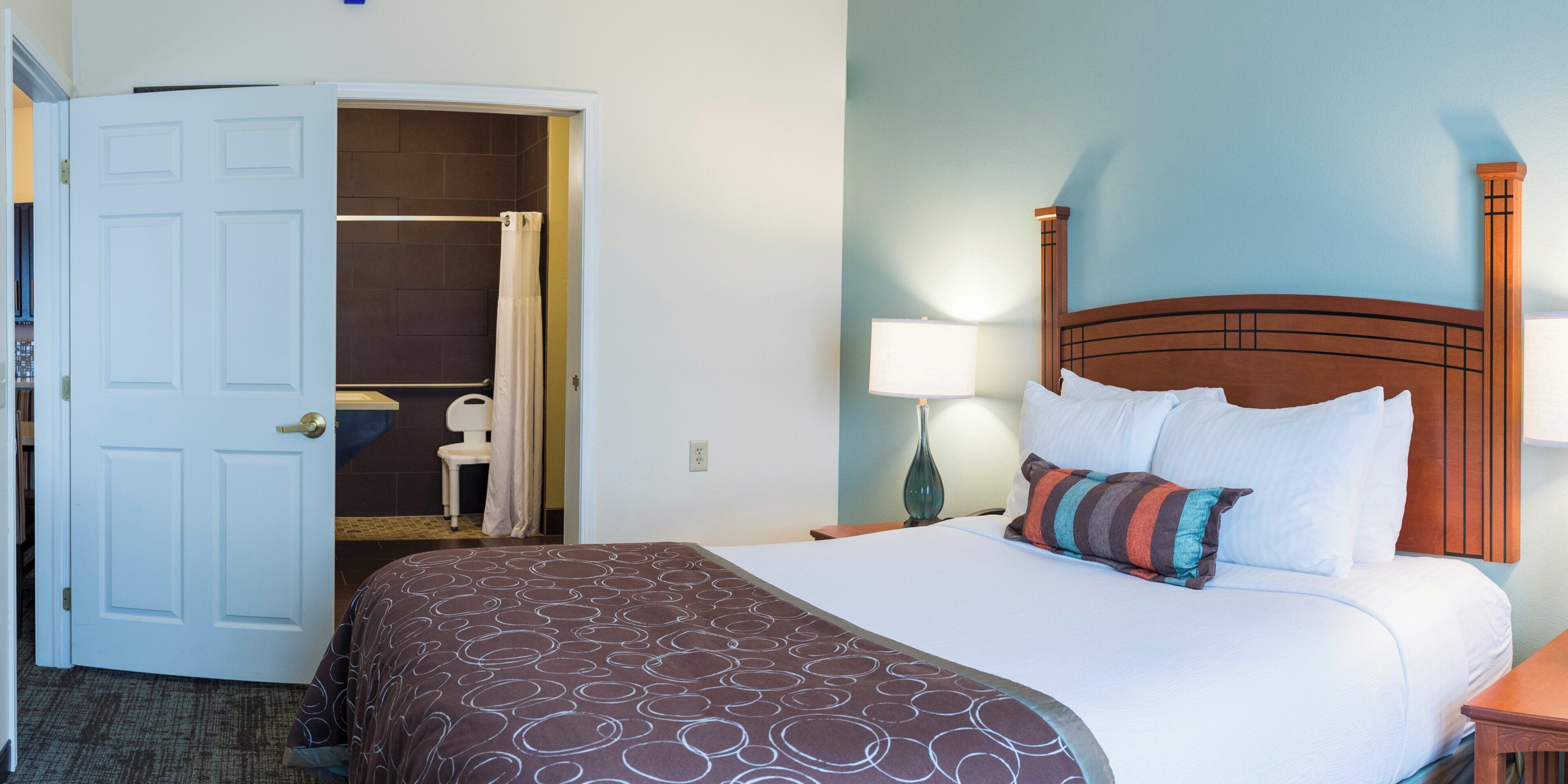A hotel room with a bed, a nightstand, a lamp, and a door leading to a bathroom.
