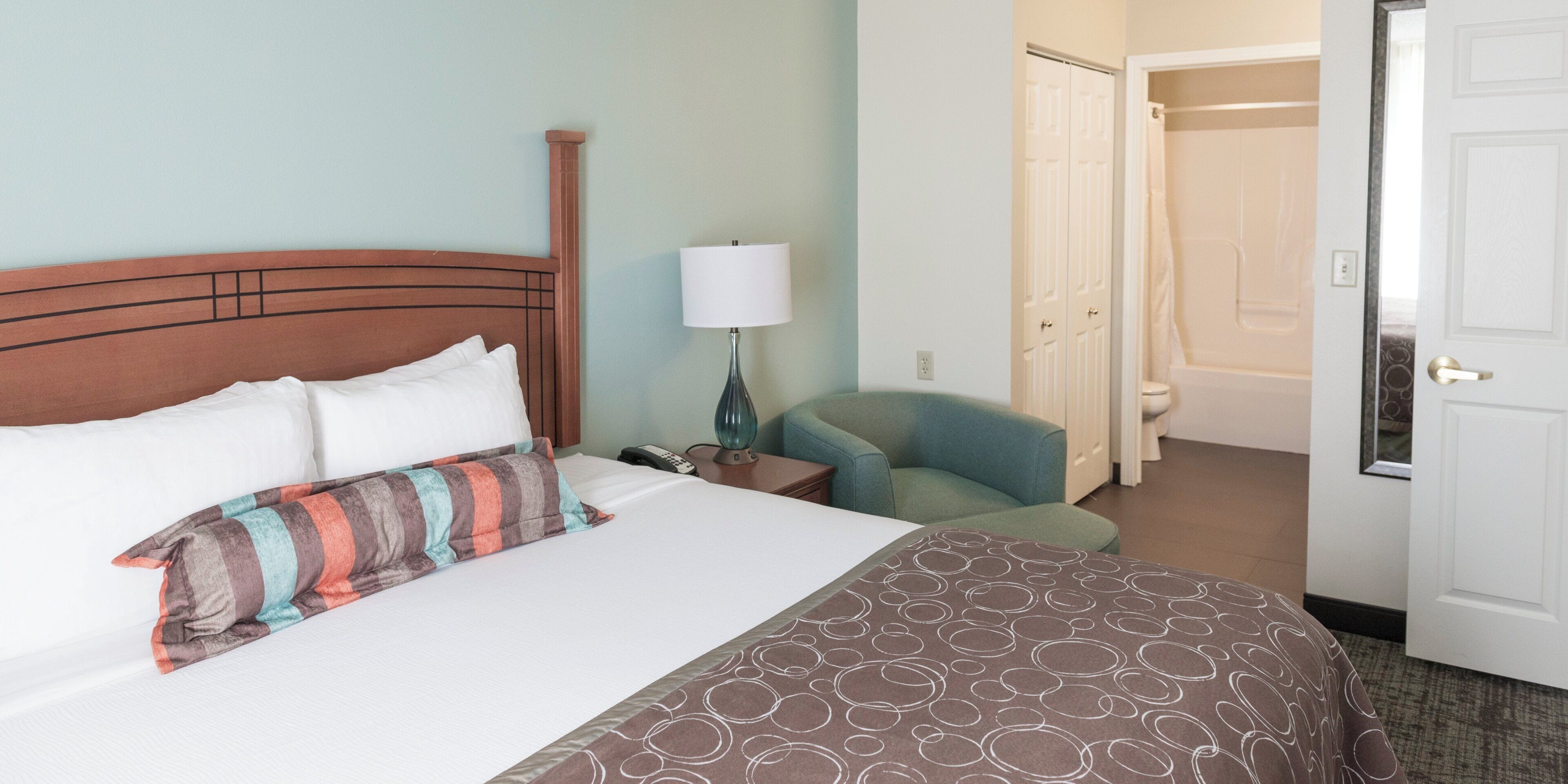 A hotel room with a bed, a chair, a lamp, and a door leading to a bathroom.