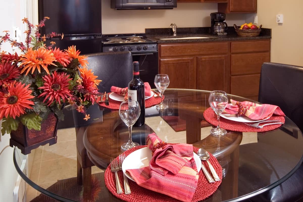 A dining area with a glass table, red placemats, and a vase of orange flowers.
