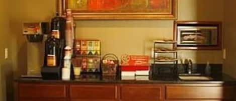A wooden cabinet with a framed painting above it, a coffee machine, and a tray of pastries.
