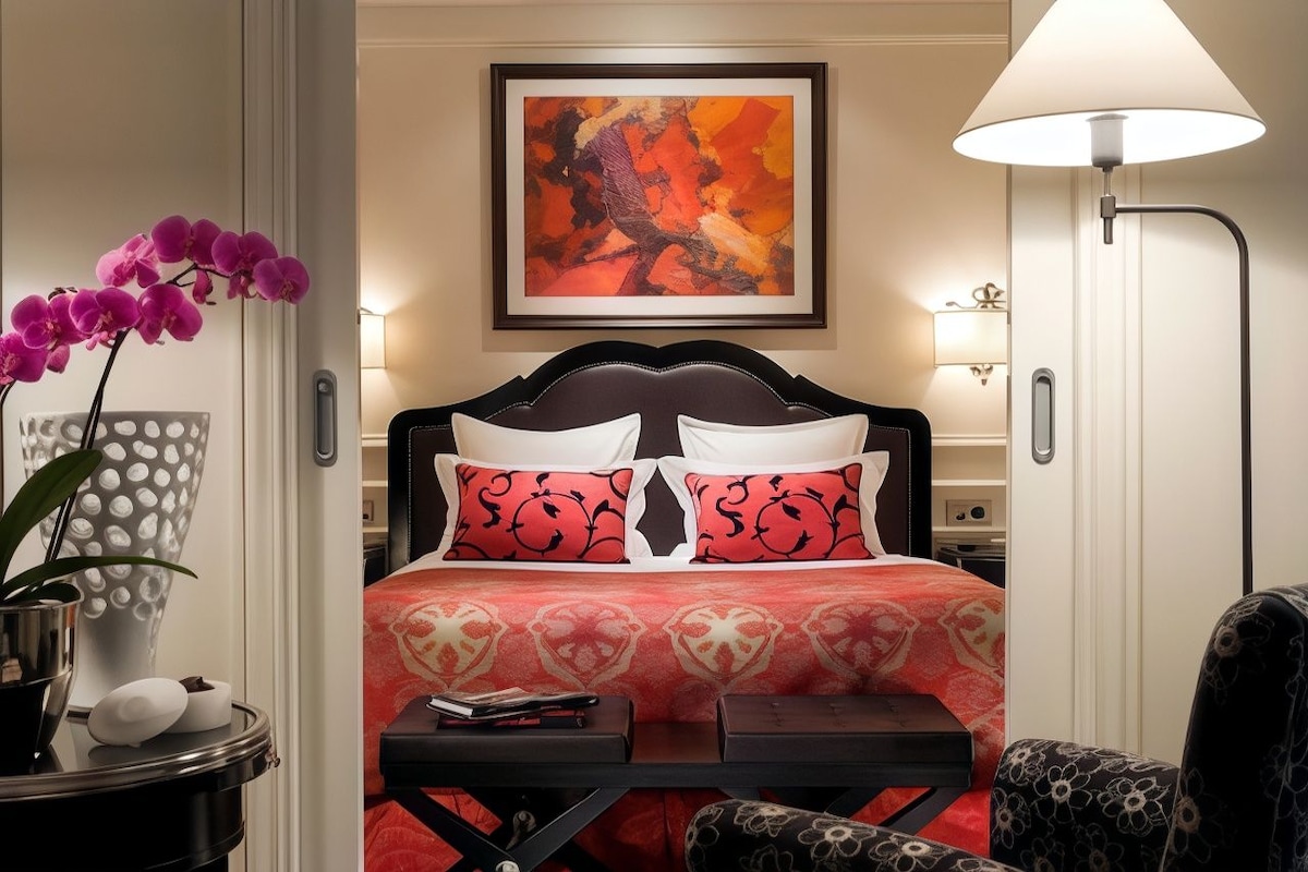 A hotel room with a bed, a bedside table, a chair, a lamp, and a painting on the wall.